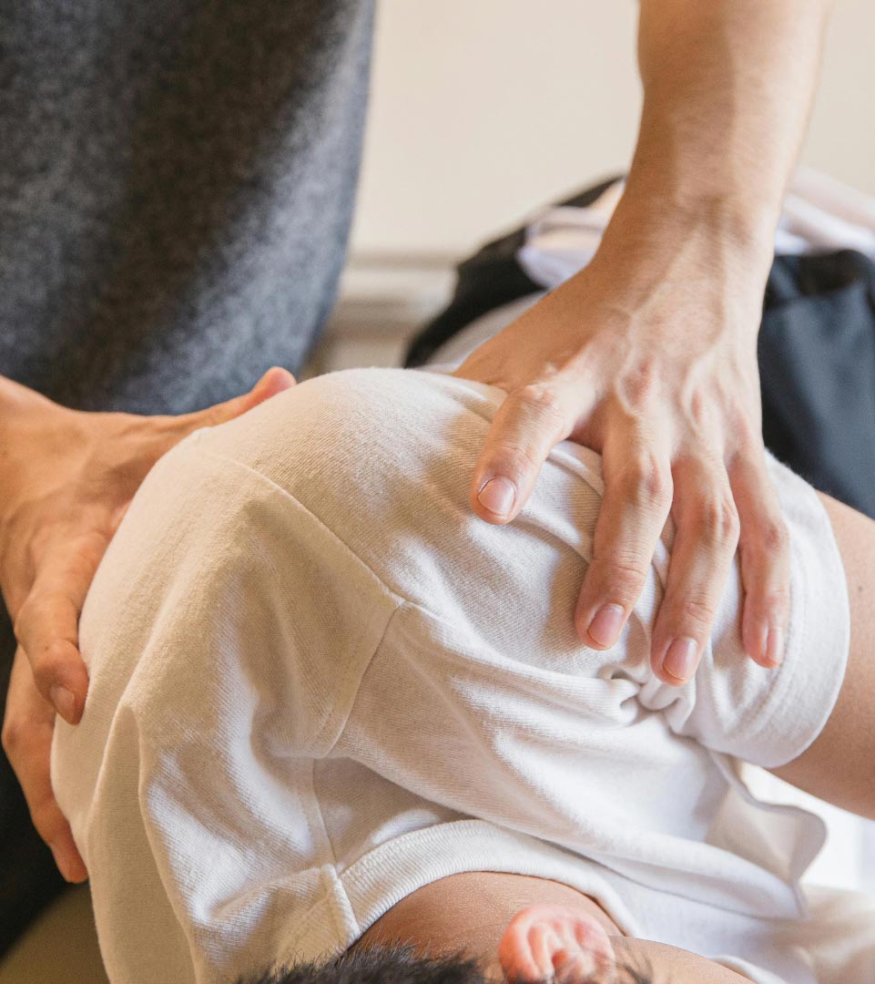 Gros plan d’une séance de thérapie manuelle où un thérapeute effectue une manipulation ou une mobilisation vertébrale sur un patient portant un t-shirt blanc.